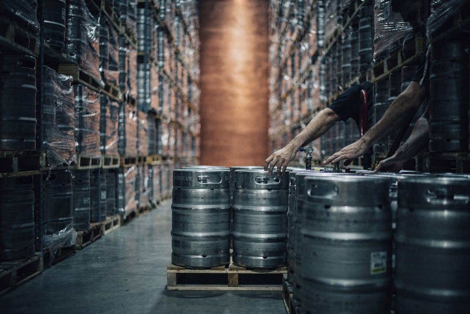 Kegs and pallets in neat aisles of a cold, orderly warehouse.
