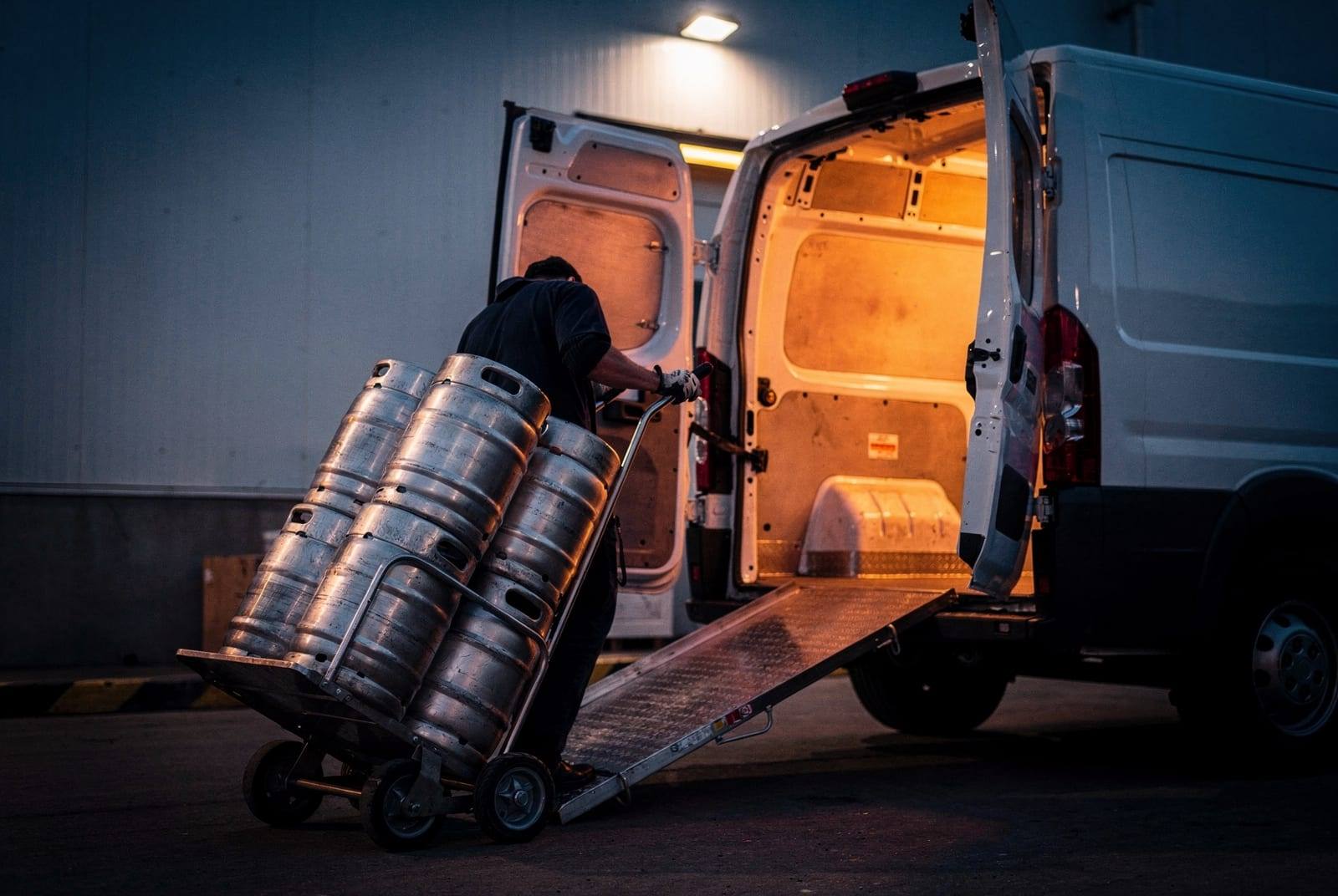 Kegs being loaded into a delivery van at dusk.